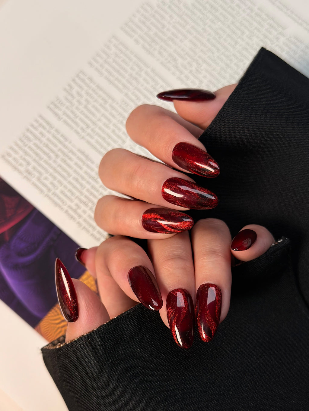 Close-up of a hand with red nail polish holding a black object against a blurred background.