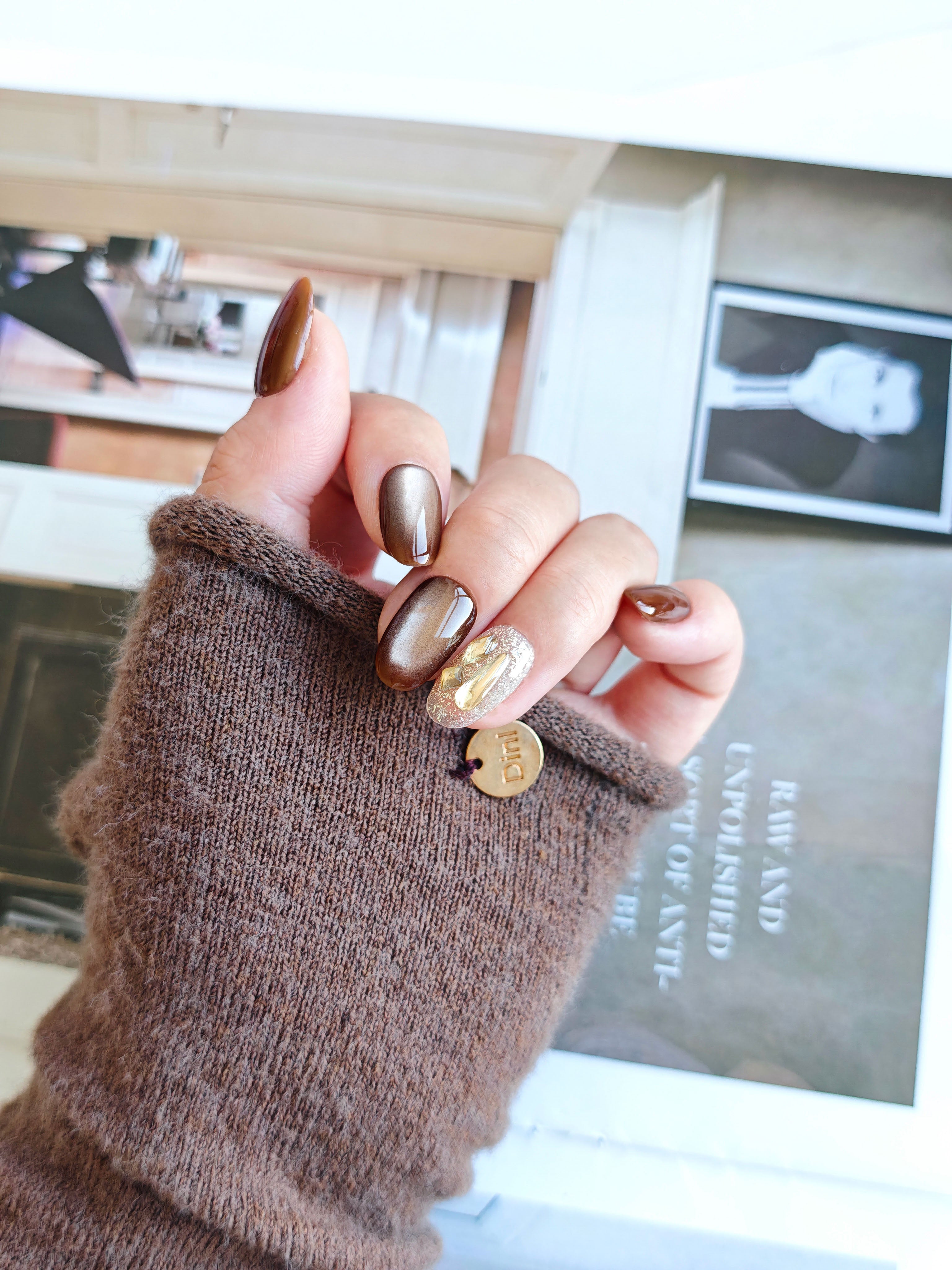 Hand with brown nail polish holding a small round object against a blurred indoor background