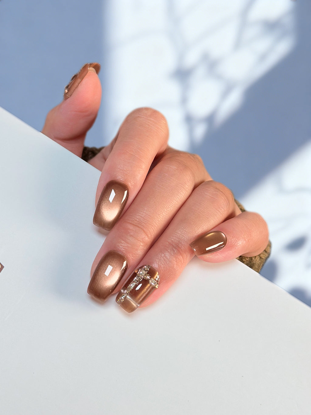 Hand with brown nail polish holding a white object against a light blue background