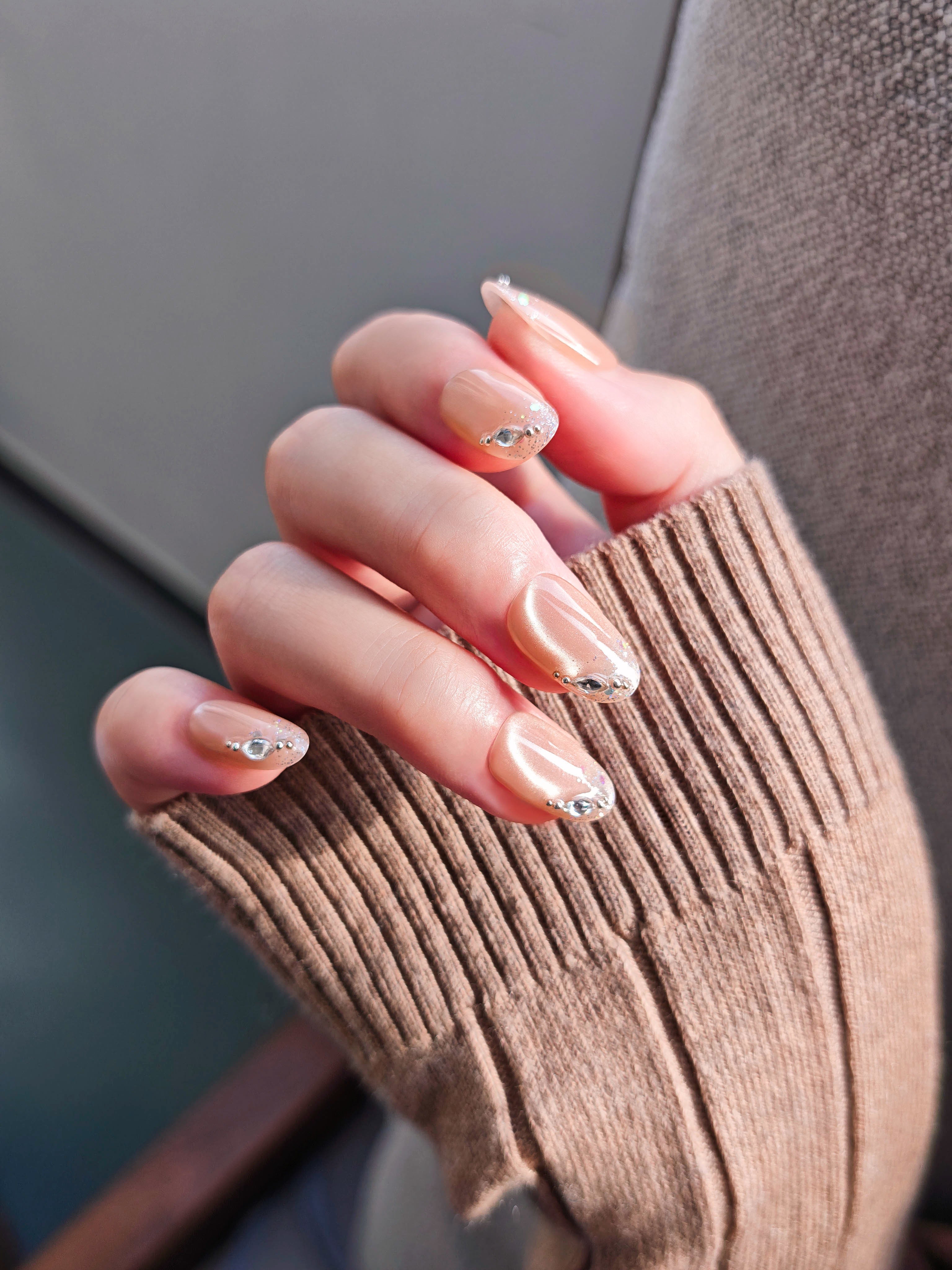Close-up of a hand with beige nail polish wearing a brown sweater.