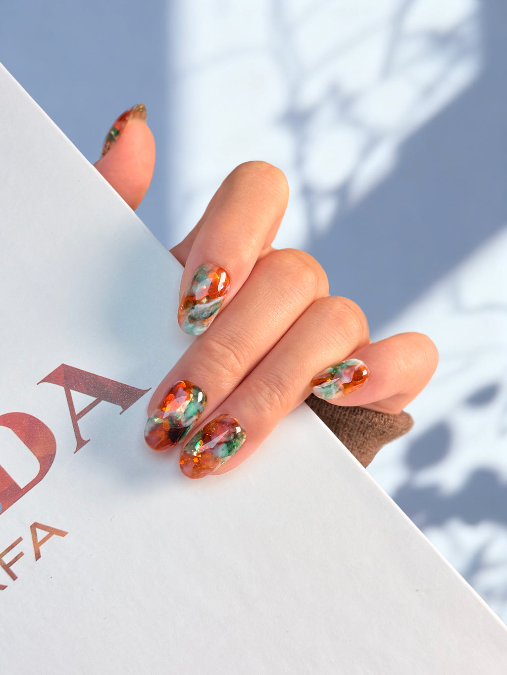 Close-up of a hand with colorful nail art holding a book against a light background