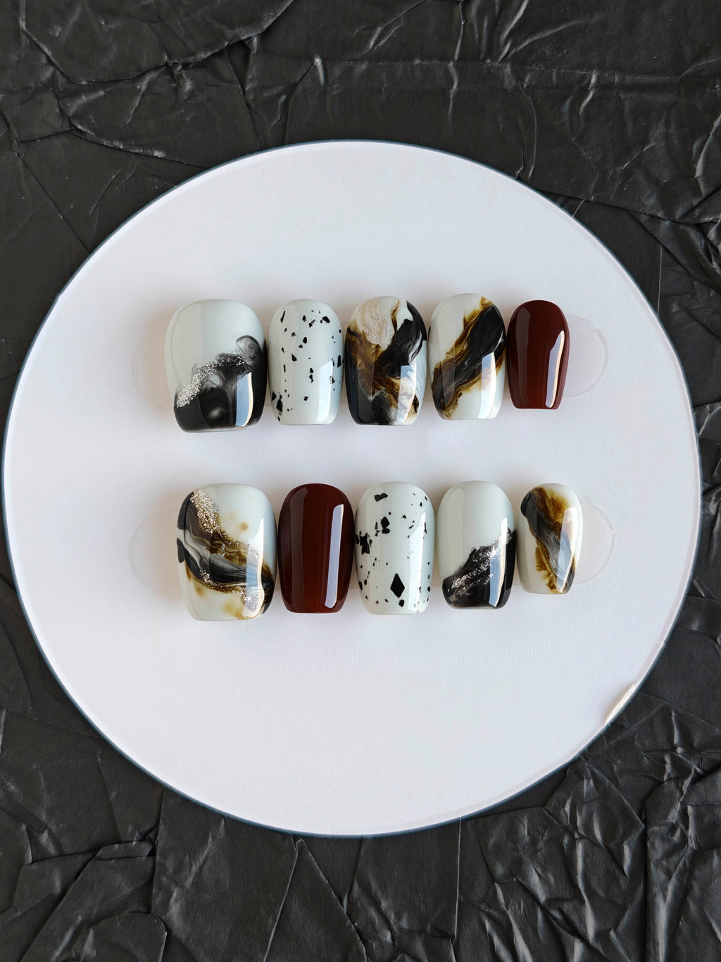 Set of marbled nail art designs on a white plate against a black textured background