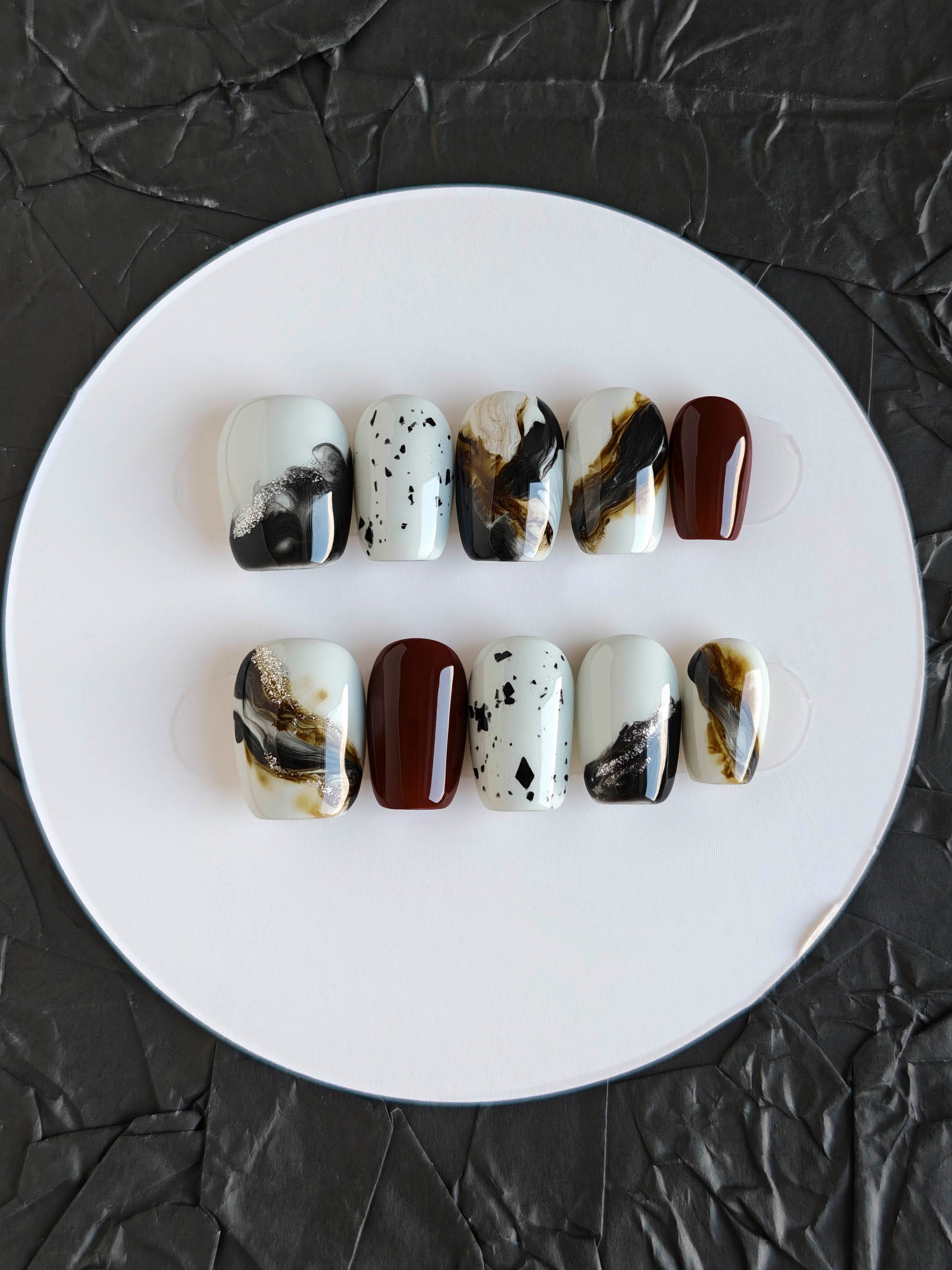 Set of marbled nail art designs on a white plate against a black textured background