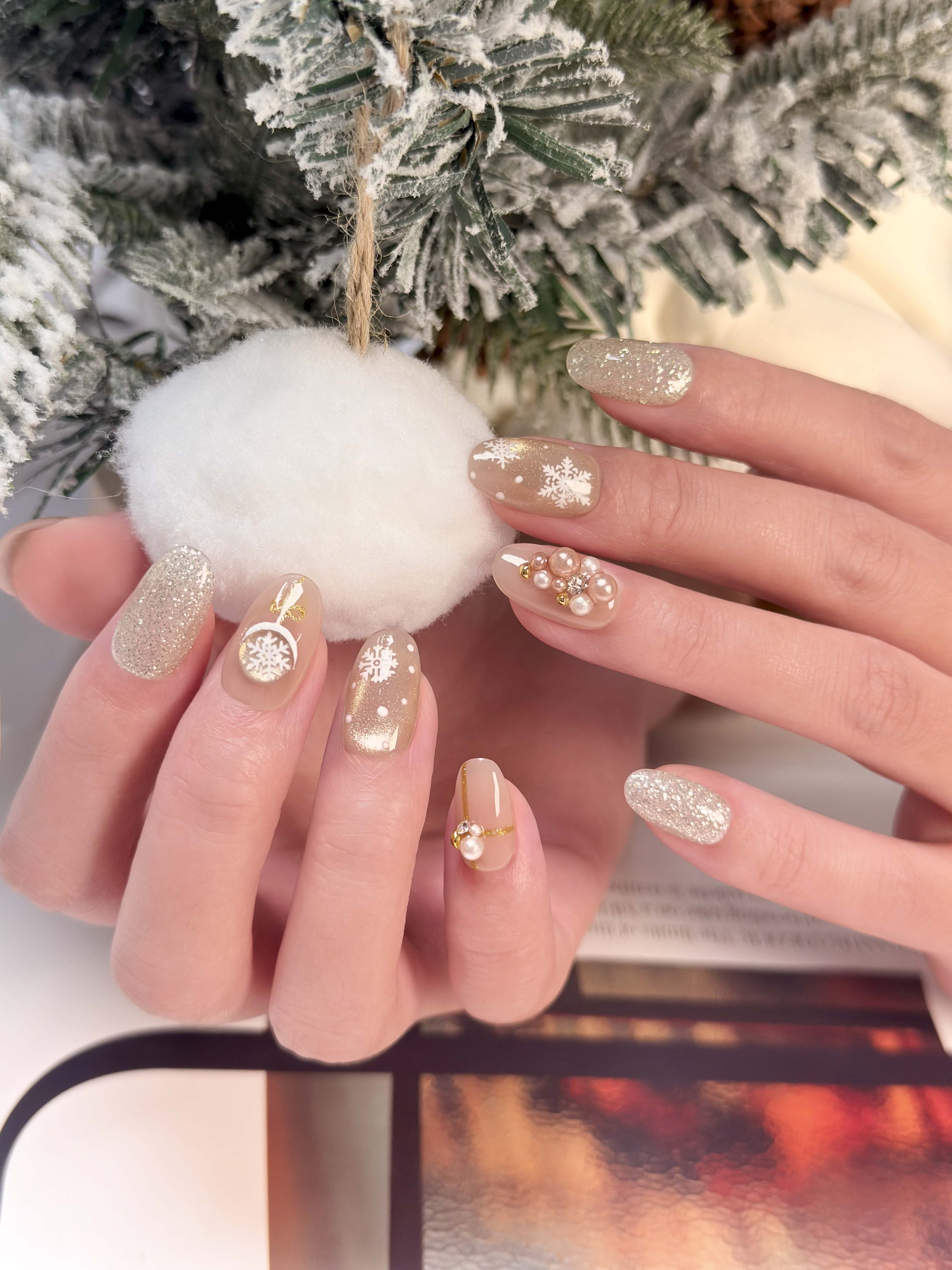 Hand with glittery nail polish holding a white ornament against a blurred Christmas tree background