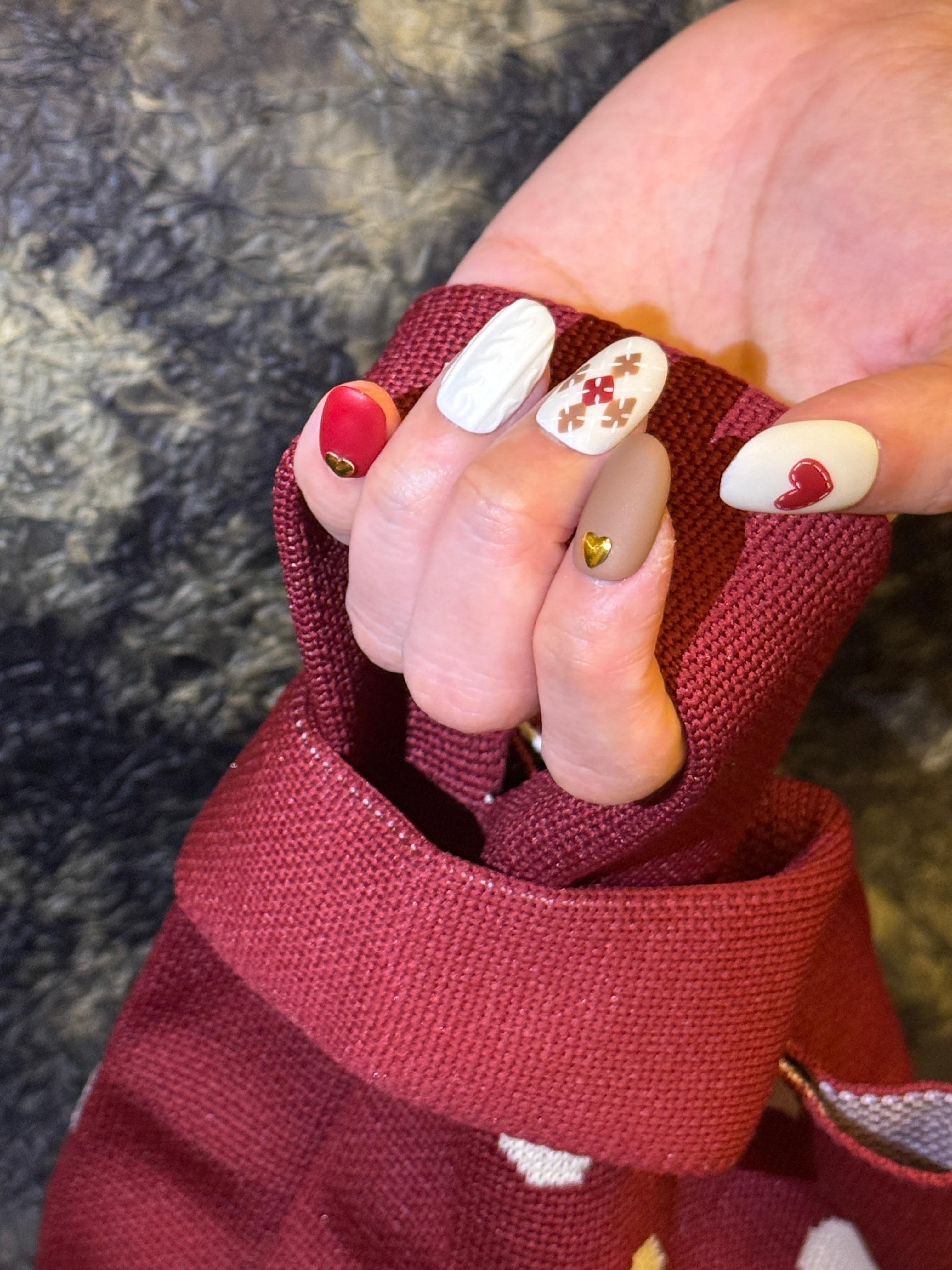 Close-up of a hand wearing a red glove with decorative nail art on a textured surface.